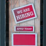 Rotes Schild an Holztür, auf dem "We are hiring" steht.