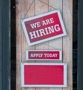 Rotes Schild an Holztür, auf dem "We are hiring" steht.